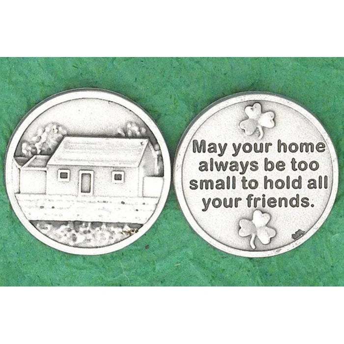 Two round silver-toned commemorative coins shown side by side on a textured green background. The left coin features an engraved house illustration, and the right coin has the phrase 'May your home always be too small to hold all your friends.