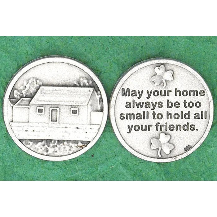 Two round silver-toned commemorative coins shown side by side on a textured green background. The left coin features an engraved house illustration, and the right coin has the phrase 'May your home always be too small to hold all your friends.