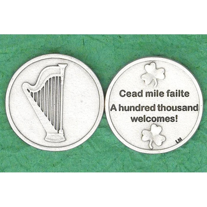 Two round silver-toned commemorative coins shown side by side on a textured green background. The left coin features a harp symbol, and the right coin has shamrocks and the text 'Cead mile failete / A hundred thousand welcomes!'.